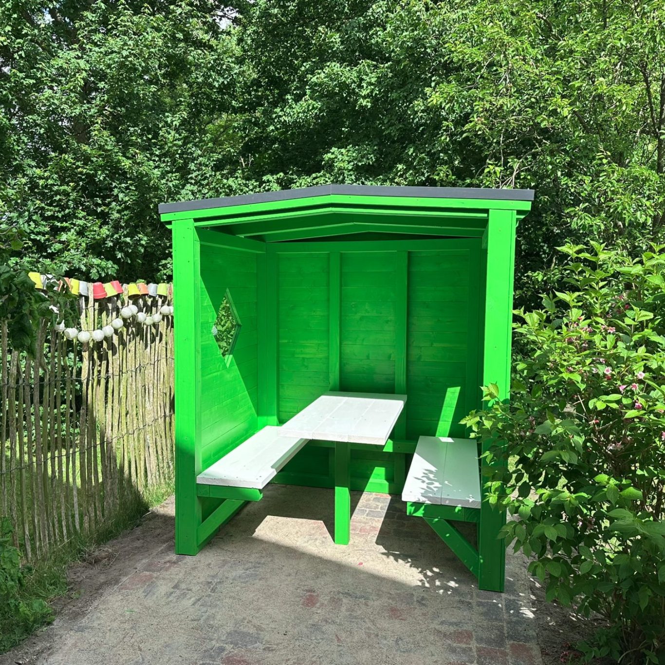 Grüne Bushaltestelle mit einer Sitzbank und umgeben von Bäumen und Sträuchern.