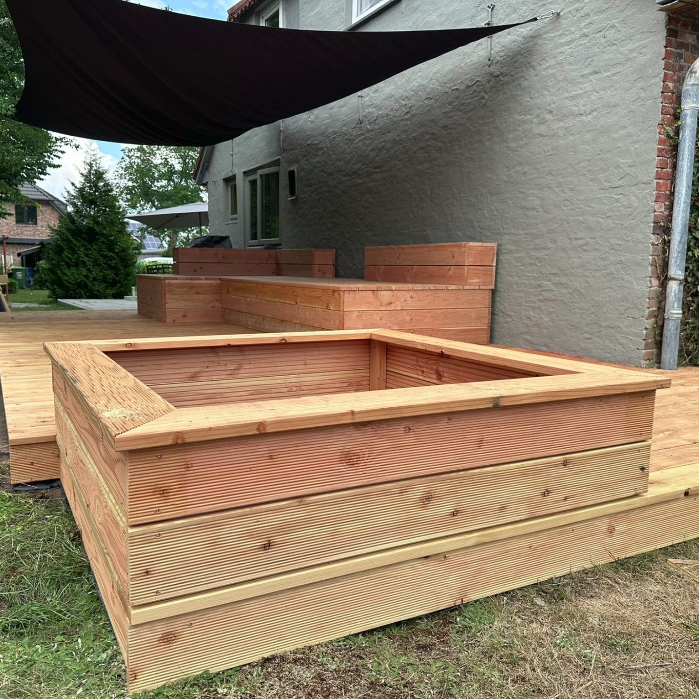 Holzkonstruktion für ein Gartenbeet mit umgebendem Holzdeck und Schattenstruktur.